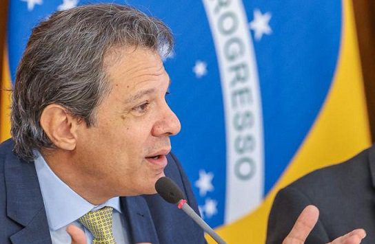 O ministro da Fazenda, Fernando Haddad, em reunião com o presidente Lula e políticas de liderança no Planalto.  Ele gesticula enquanto fala diante do microfone - Metrópoles